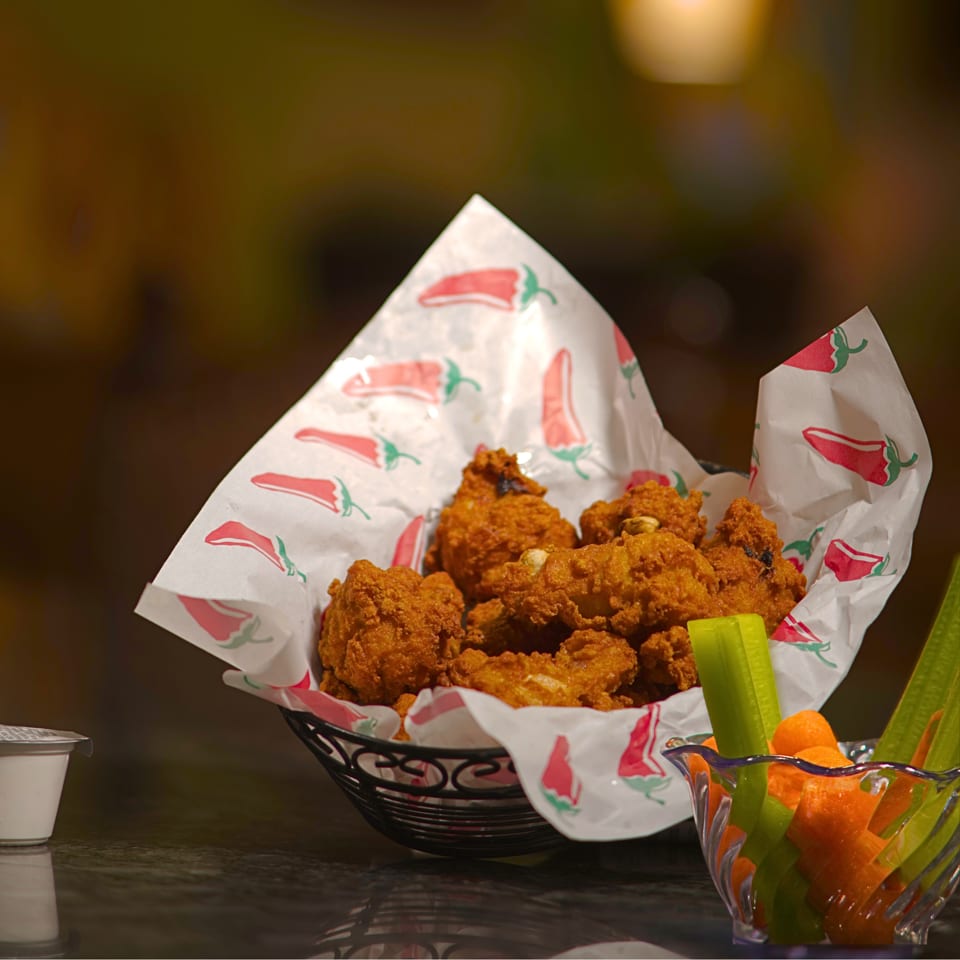 Basket of crispy fried chicken served with celery and carrot sticks in a warmly lit restaurant.