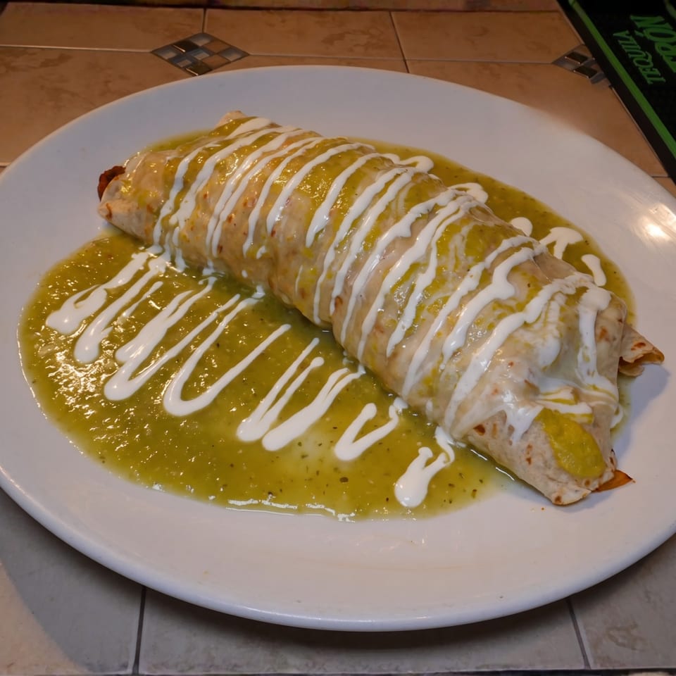 Large burrito covered with green sauce and white crema on a white plate.