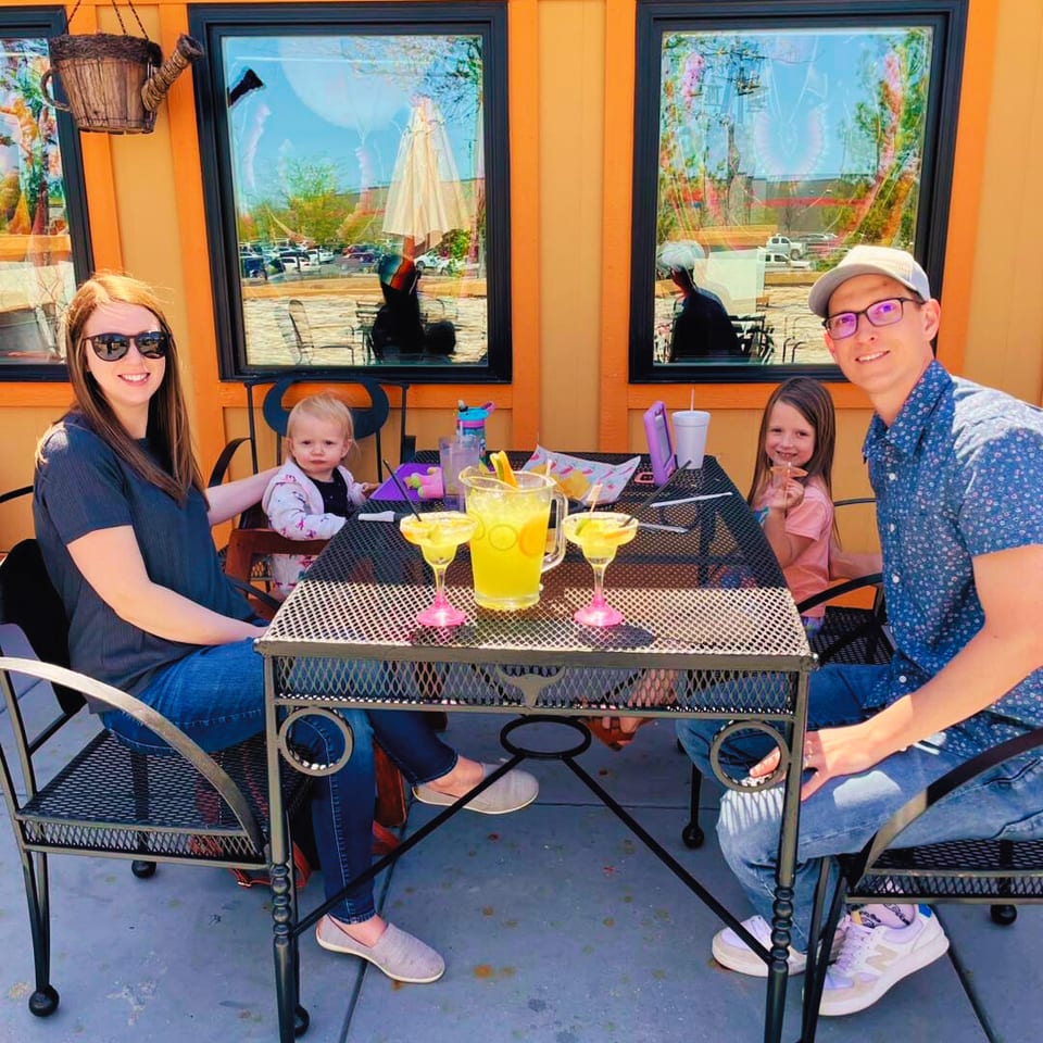 Family of four, including two young children, enjoying drinks at an outdoor restaurant table.