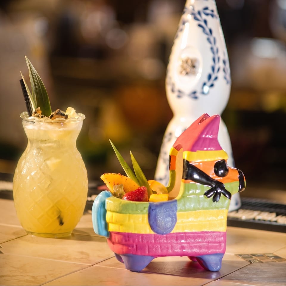 Tropical fruit drink beside a colorful donkey-shaped serving dish and patterned ceramic bottle on a restaurant table.