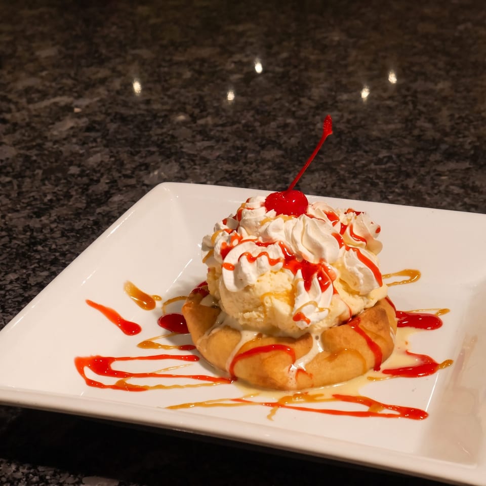Dessert topped with whipped cream and a cherry, drizzled with red and caramel sauces on a white platter.