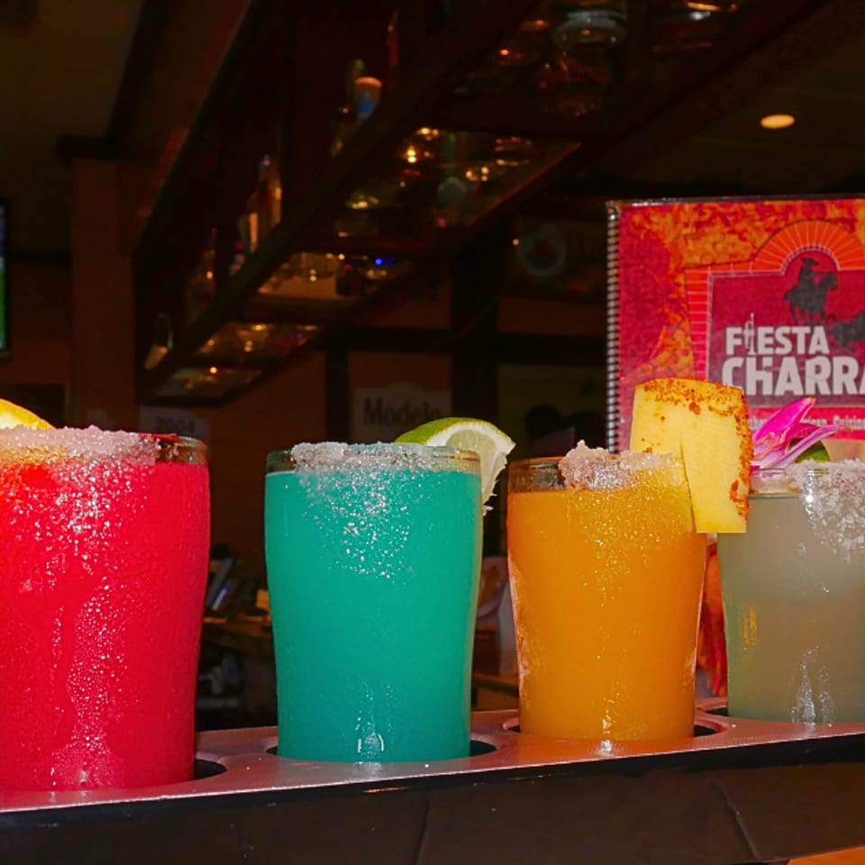 Four colorful margaritas with salted rims and fruit garnishes on a tray at Fiesta Charra.