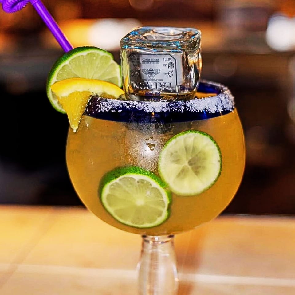 Margarita with lime slices, orange wedge, purple straw, and a Patron tequila shot on top.