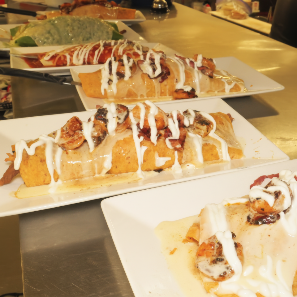 Assorted sushi rolls on white plates, topped with creamy white sauce, arranged across a restaurant counter.